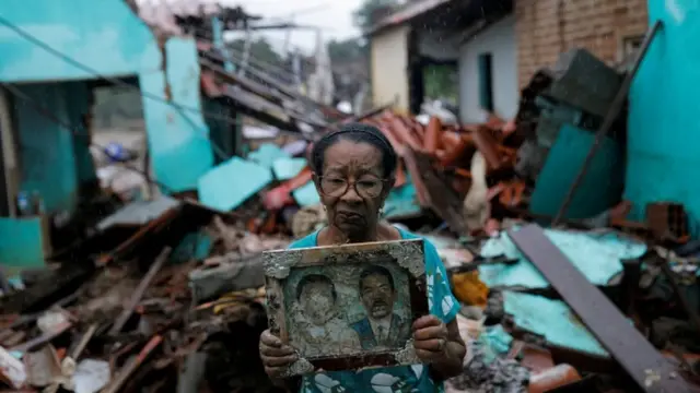 Imagen de una mujer frente a una residencia destruida