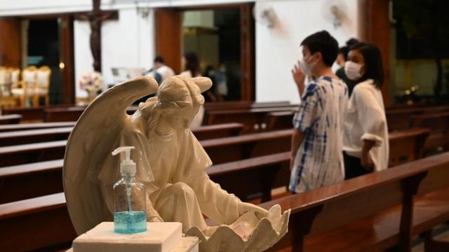 A bottle of hand sanitizer at the entrance of a church in Bangkok, with worshippers wearing face masks in background