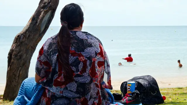 बीच किनारे बैठी महिला की तस्वीर पीछे से