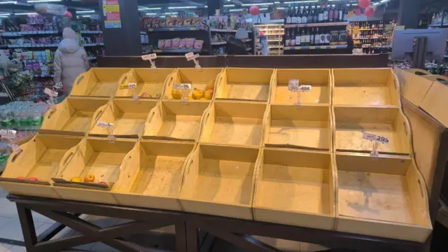 Пустой стенд в супермаркете. В отсеках есть несколько яблок, все остальное раскупили