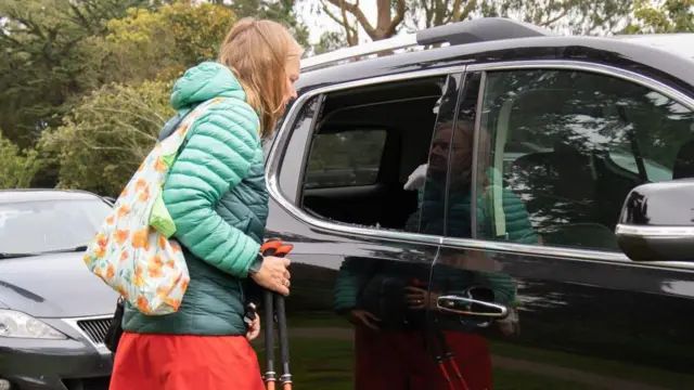 Une femme regarde une voiture dont la vitre arrière est cassée.