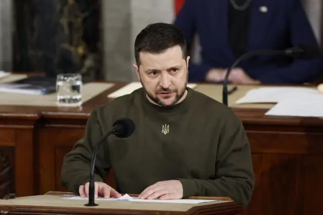 Зеленський у светрі кольору хакі перед мікрофоном