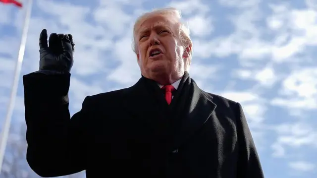US President Donald Trump wearing a black overcoat, black gloves and red tie speaks to members of the media on the South Lawn of the White House before boarding Marine One in Washington, DC, US, on Tuesday, Jan. 27, 2026. 