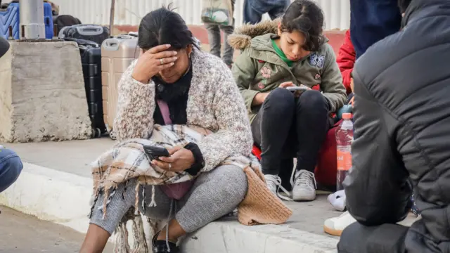 Migrantes varados en la frontera entre México y EE.UU. miran sus celulares