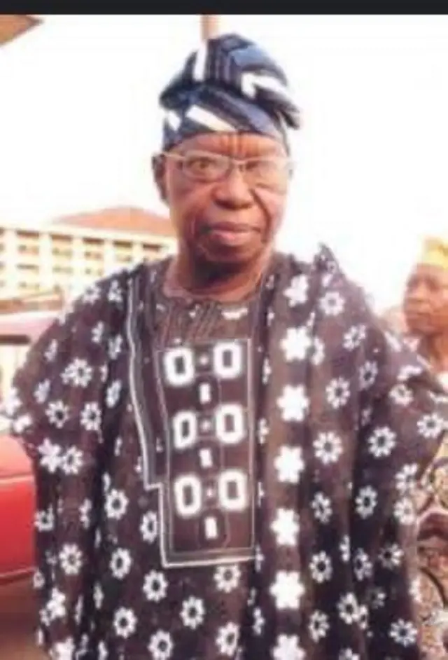 Oloye Lere Paimo dúró, wọn wọ aṣọ agbada olómi Kọfi, wọn si de fìlà aṣọ náà. Wọn lo awo oju. 