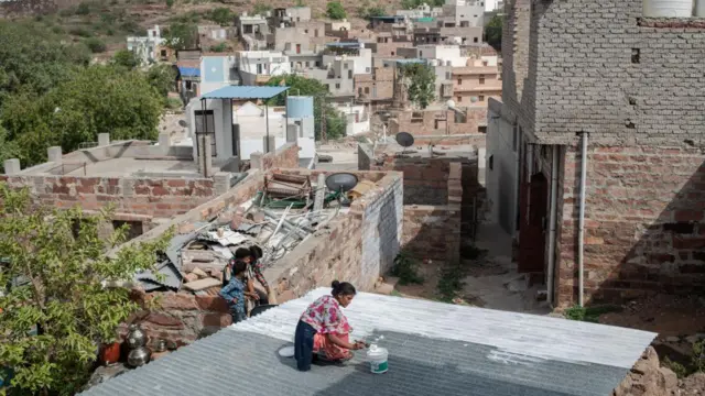 Seorang perempuan di Chandpole, Jodhpur, India, mengecat atap rumahnya dengan cat reflektif berwarna putih. 