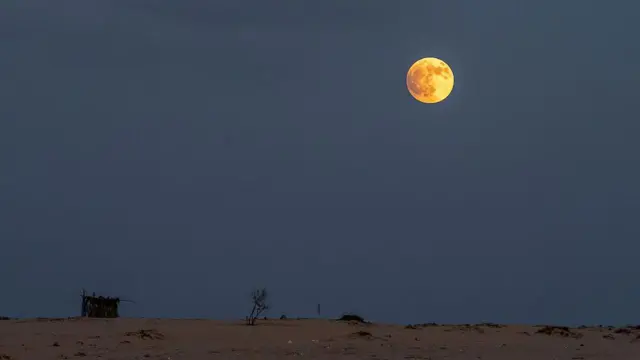 Uma lua vermelha brilhante no alto de um céu nublado e pálido acima de um deserto arenoso