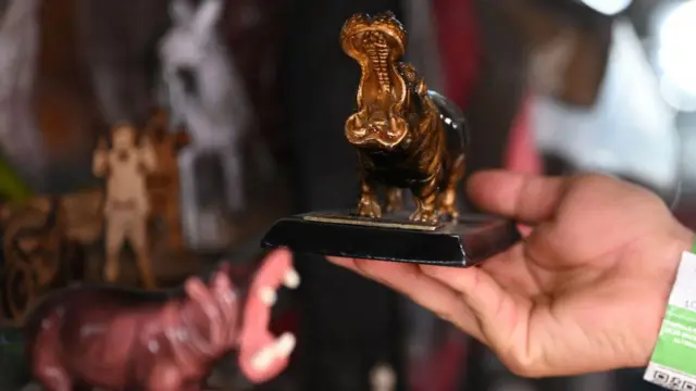 Чоловік тримає фігурку бегемота в сувенірній крамниці в Колумбії. Ще одну фігурку видно на задньому плані