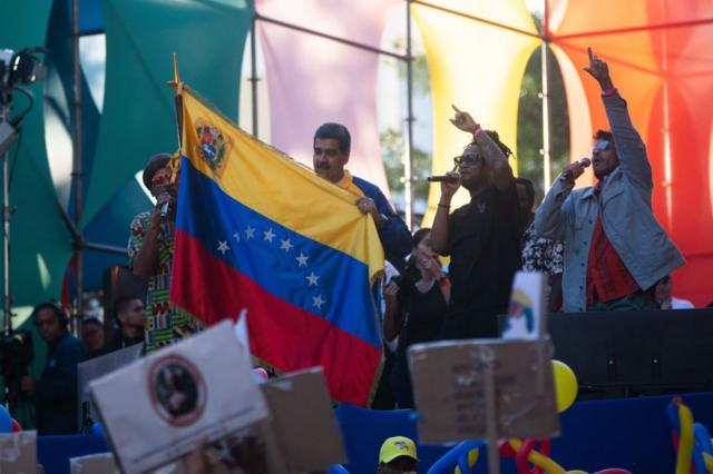 Maduro em comício, sorrindo e segurando bandeira da Venezuela
