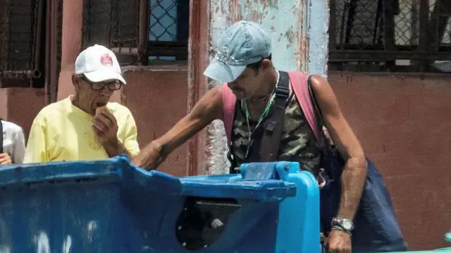 Un mendigo revisando un contenedor de basura