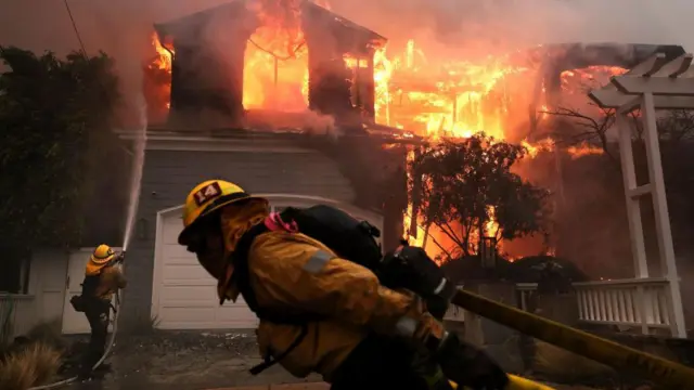 Bomberos intentan apagar el fuego en una casa en Palisades