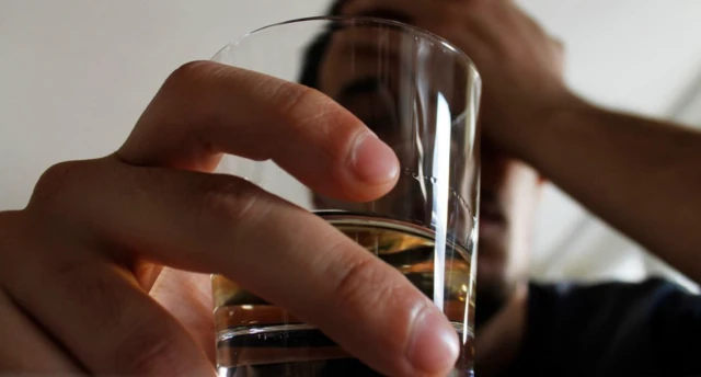 Elinde alkolle başını içmek istemez gibi tutan bir kişi