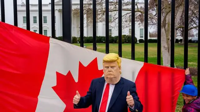 Na frente da Casa Branca, em Washington, homem usa máscara com rosto de Donald Trump com uma bandeira canadense ao fundo