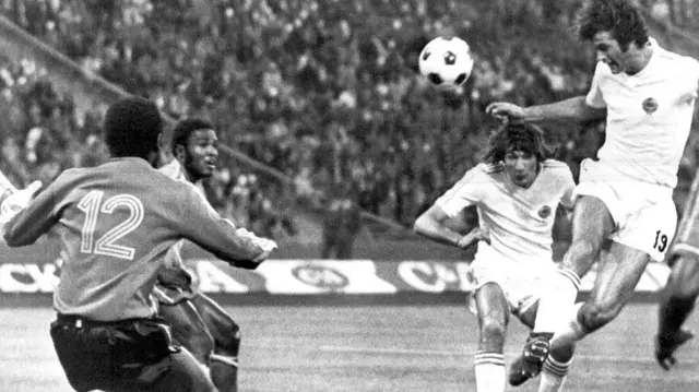 لاعبو مباراة الزائير ويوغوسلافيا في نهائيات كأس العالم 1974، على الجانب الأيمن لاعبين يحاولان التقاط الكرة، وعلى الجانب الأيسر لاعبين يحاولان منع مرورهما