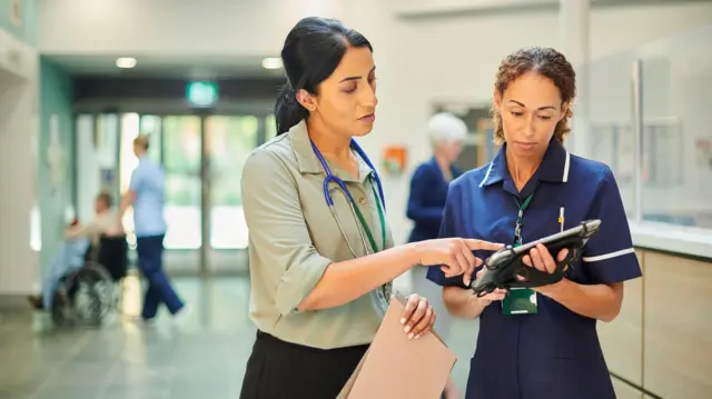 Una médica y una enfermera revisando la base de datos de registros médicos.