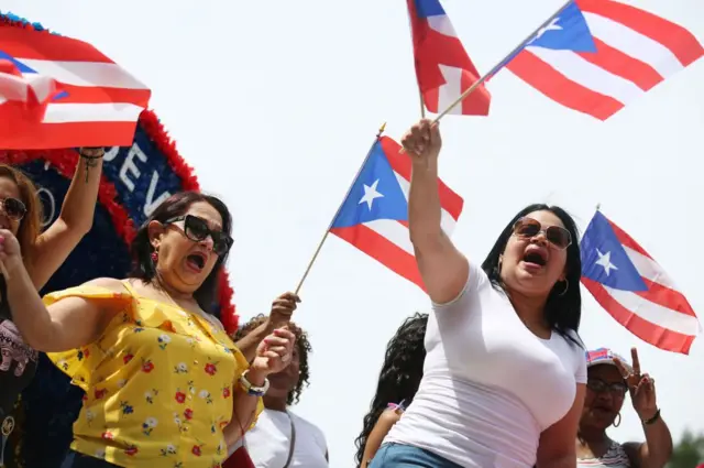 Dos mujeres ondean banderas de Puerto Rico en un desfile en Boston. 