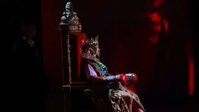 تایسون فیوری در حالی که تاج روی سر گذاشته بودند و روی تخت طلا نشسته بودند، به سوی رینگ برده شد