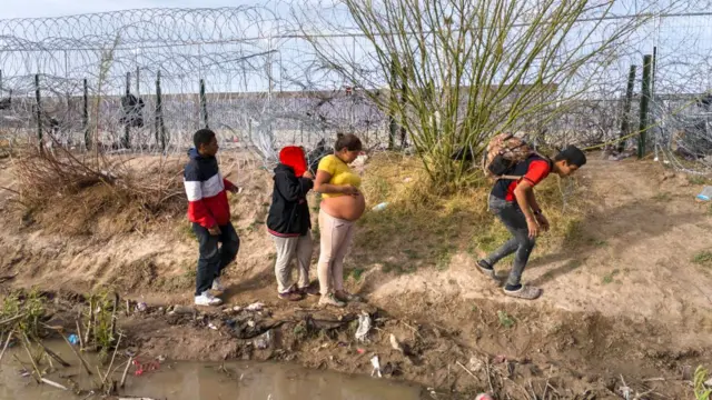 Uma mulher grávida da Venezuela e outros migrantes caminham ao longo das margens do Rio Grande depois de cruzar a fronteira entre os EUA e o México em 13 de março de 2024 em El Paso, Texas. 