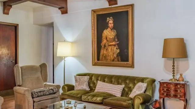 Sala de estar com um sofá verde contra uma parede branca, com um abajur de cada lado e um retrato pendurado na parede atrás do sofá