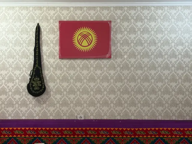 Duvara asılmış Kırgızistan bayrağı ve Orta Asya Türklerinin milli çalgısı kopuz.