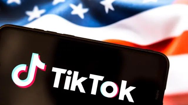 Logo do TikTok em celular, com bandeira dos EUA atrás do aparelho