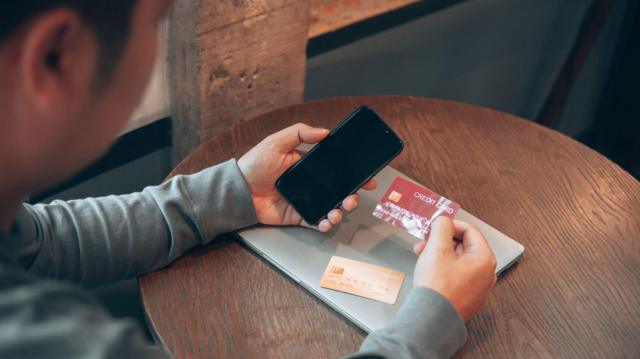 Pessoa segurando celular e cartão de crédito