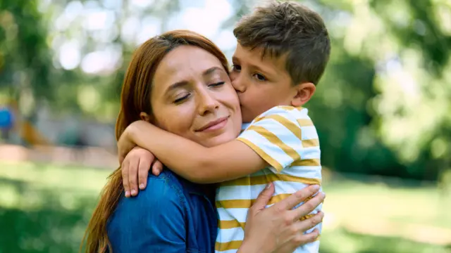 Szczęśliwa mama i syn spędzają piękny dzień w parku, dzieląc czuły moment pełen miłości i bliskości, gdy dziecko całuje i przytula swoją mamę.