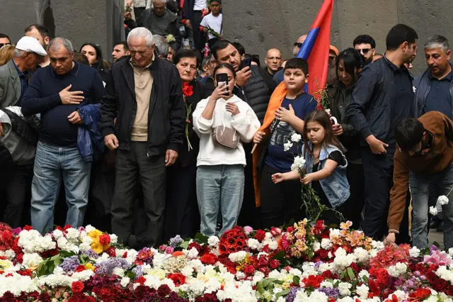 Çiçeklerin önünde elini kalbine koymuş bir adam, çocuklar, Ermenistan bayrağı