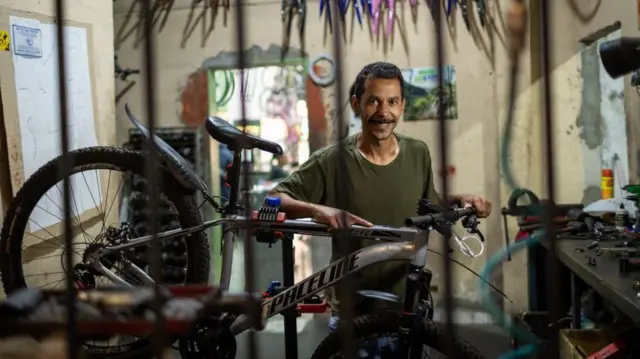 Fernando é um homemapostas esportivas pdfpele morena, com camiseta verde-escuro. Está mexendoapostas esportivas pdfuma bicicleta e sorrindo para a foto.