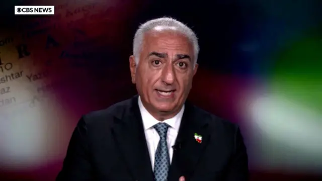 白髪の男性がカメラに向かって話している。スーツの襟にイランのピンバッジがついている