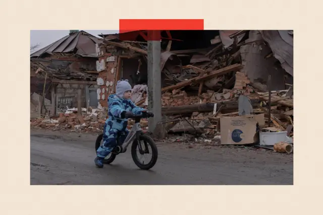 Ребенок едет на велосипеде возле разрушенных домов в Золочеве, Харьковская область, Украина.