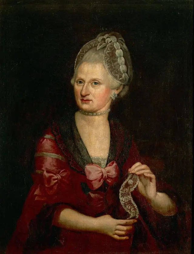 Retrato de Anna Maria Mozart, elegantemente vestida con un vestido rojo oscuro, con un lazo en el centro y con una especie de cinta en la mano.