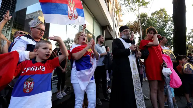 A Serbian orthodox priest and supporters of Serbia's Novak Djokovic gather during a prayer outside a government detention centre where the tennis champion is reported to be staying in Melbourne on 7 January 2022