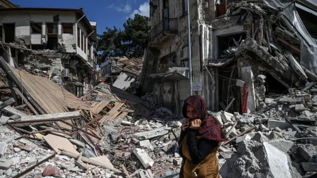 Seorang perempuan berdiri di antara reruntuhan bangunan di Hatay pada 6 Maret 2023, satu bulan setelah gempa bumi besar melanda Turki bagian tenggara.