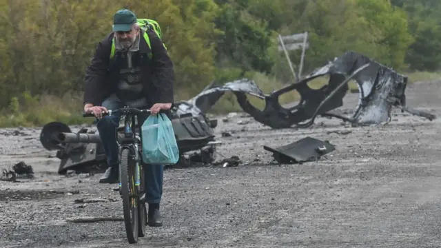 ख़ार्किएव के बालाक्यिा में सैन्य उपकरणों के मलबे से लदी सड़क पर गुज़रता साइकिल सवार