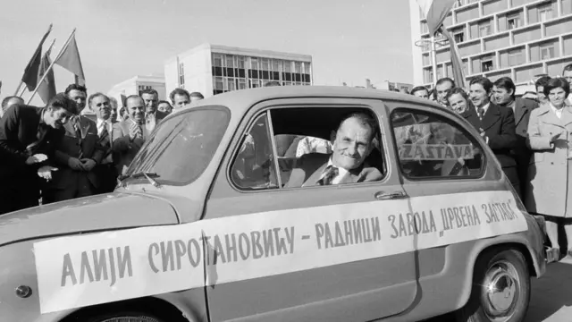 Alija Sirotanović viri iz fiće, oko njega su okupljeni ljudi koji tapšu