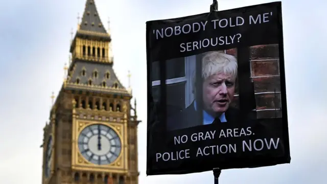 Um manifestante segura um cartaz mostrando o primeiro-ministro britânico Boris Johnson, do ladofora do parlamentoLondres, 19janeiro2022