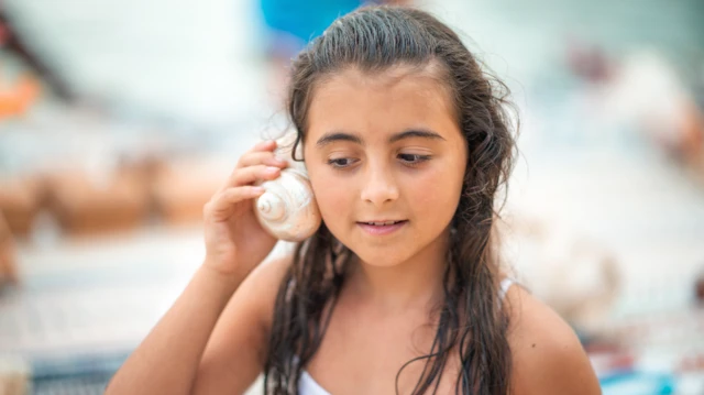 Une jeune fille tenant un coquillage à son oreille à l'île Maurice