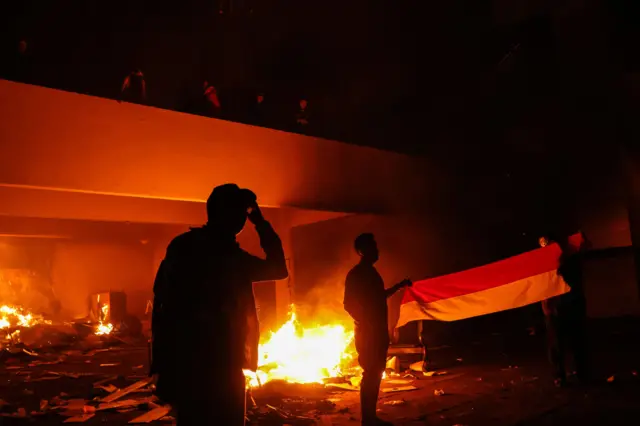 Pengunjuk rasa membentangkan umbul-umbul merah putih di depan gedung DPRD Sulawesi Selatan yang dilalap api saat aksi 29 Agustus di Makassar, Sulawesi Selatan, Sabtu (30/8/2025) dini hari. 
