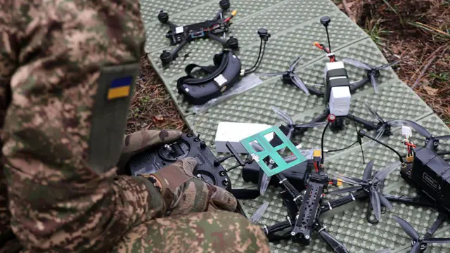 На карематі перед оператором з пультом керування розкладені FPV-квадрокоптери 