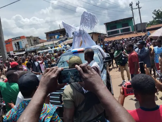 Crowd gather dey watch vehicles wey dey pass during di burial of late Mr Ibu