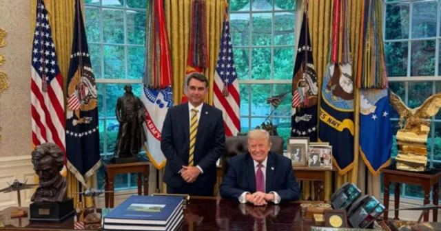 Flávio Bolsonaro de terno, em pé, no salão oval da Casa Branca, com Donald Trump, à direita, sentado. Ambos estão sorrindo