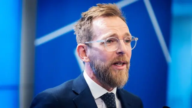 O ministro da Saúde da Suécia, Jakob Forssmed, de terno e óculos, com fundo azul