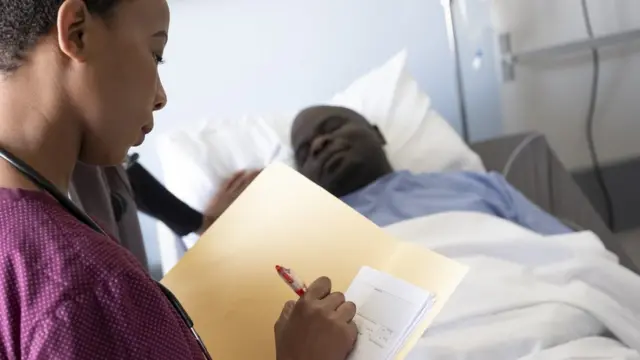 Un patient alité avec un soignant écrivant sur sa fiche.