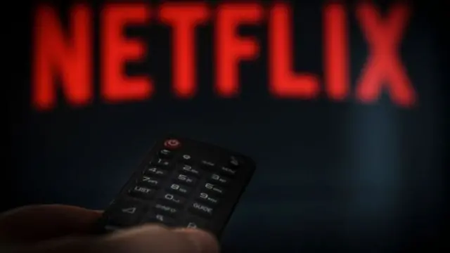 Mão com controle remoto e logo do Netflix ao fundo