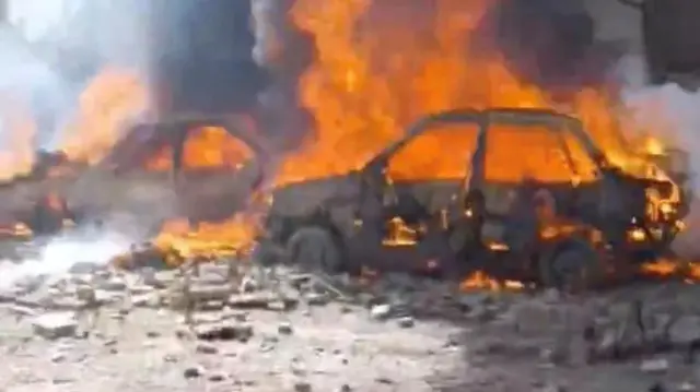 日中の道路で複数の車両が燃え、周りにがれきが散らばっている