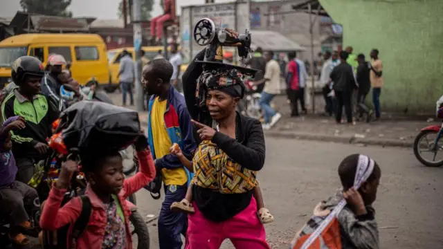 One woman carry sewing machine on her head plus oda belongings as she run from Kibati, wia fighting don catch fire, dey go di city of Goma on January 26, 2025.
