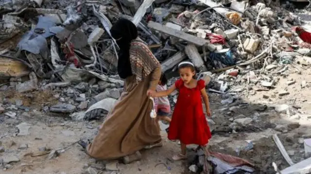 سيدة تصطحب ابنتيها وتحاول أن تمضي وسط أنقاض الحرب في غزة