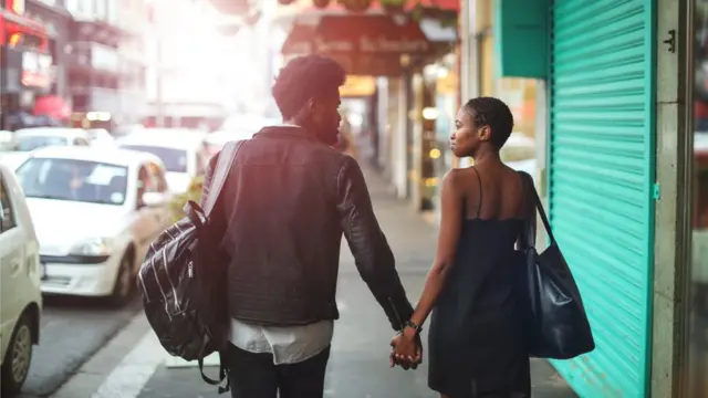 A man and a woman walk away from the camera down a city street