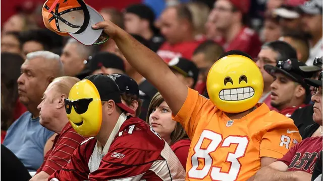 Hombre lleva máscara de un emoji en un partido de beisbol